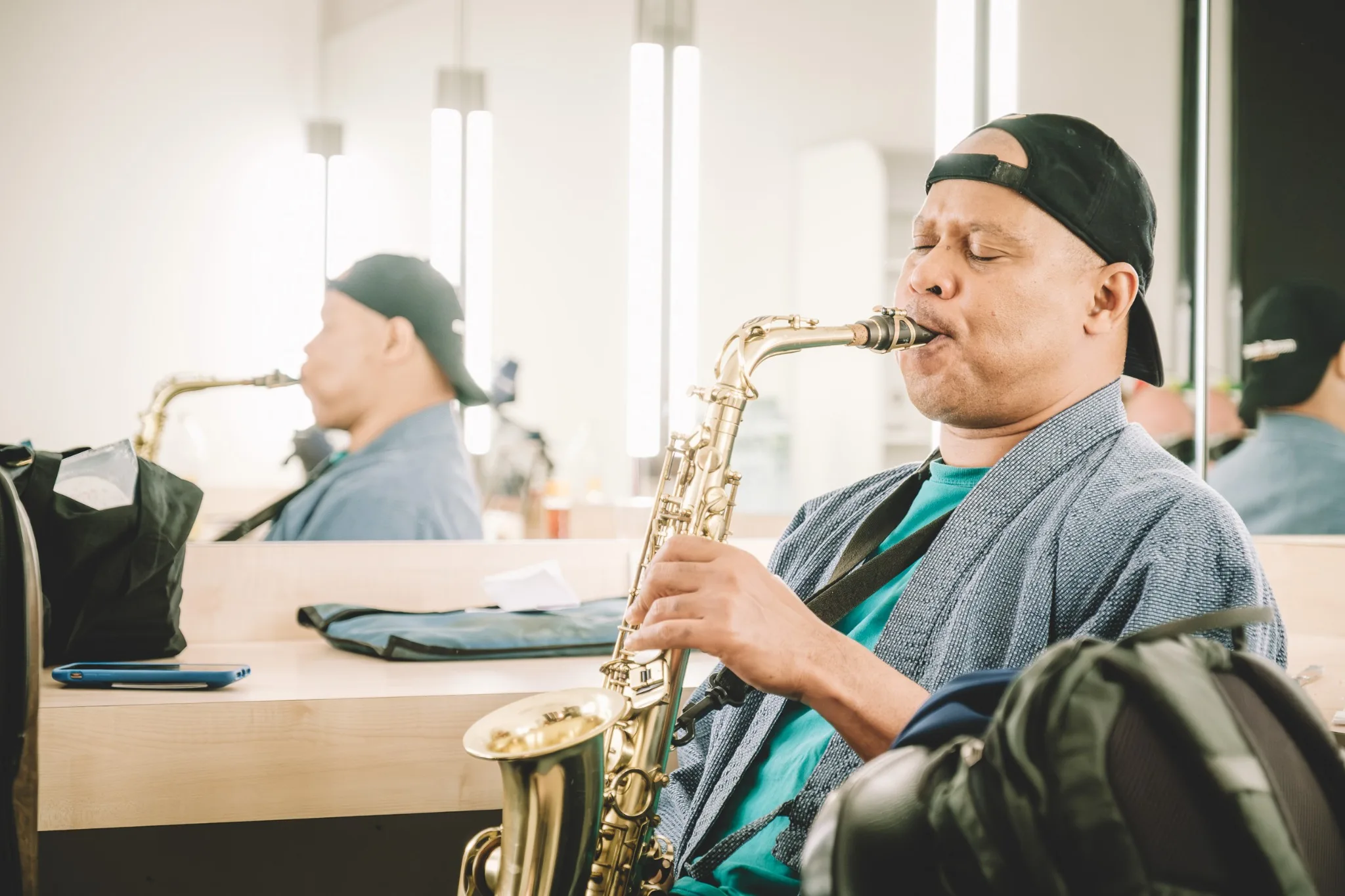 Steve Coleman playing alto saxophone in front of a dressing-room mirror.