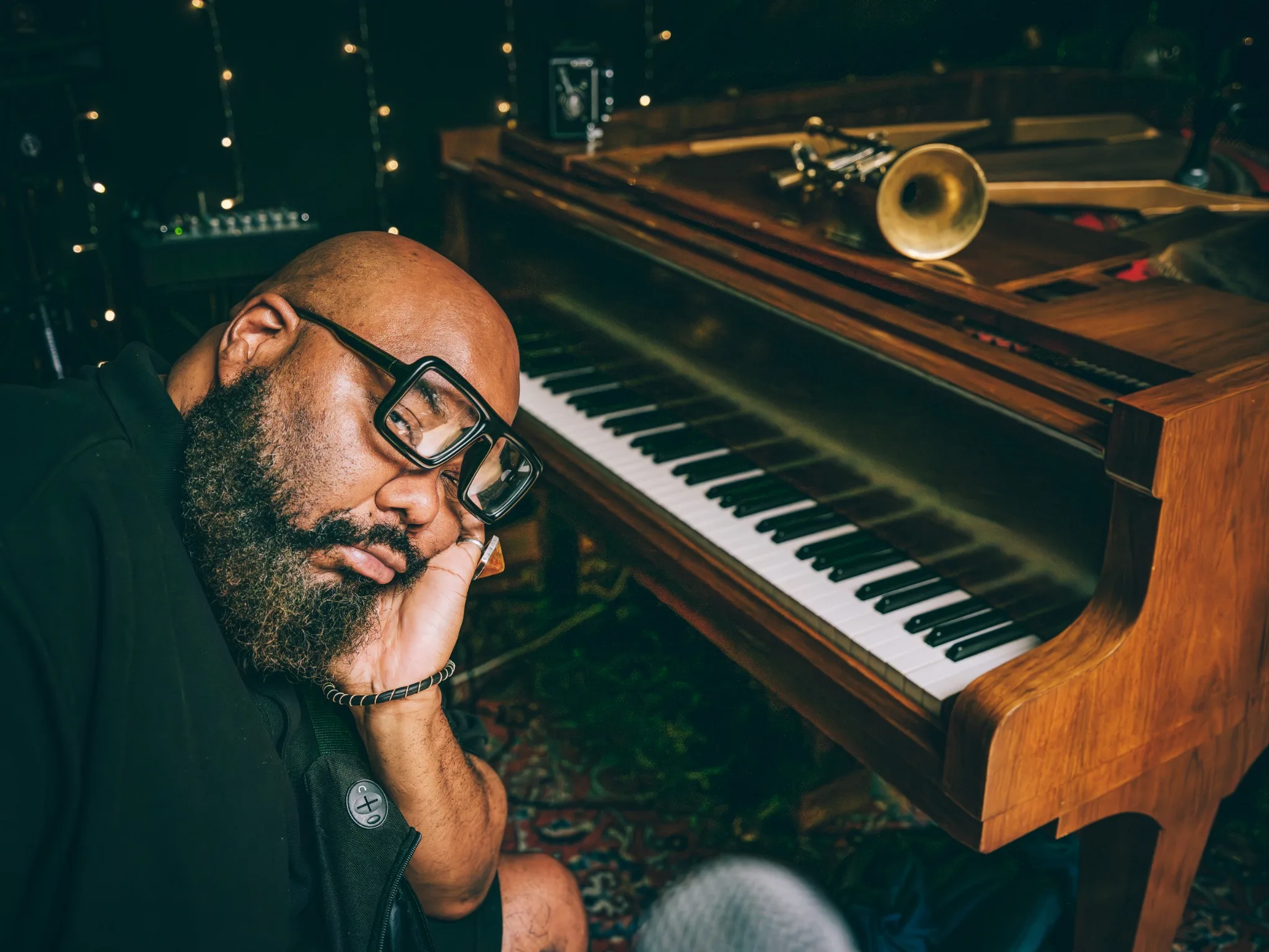 Kokayi resting his head on his hand beside a piano.