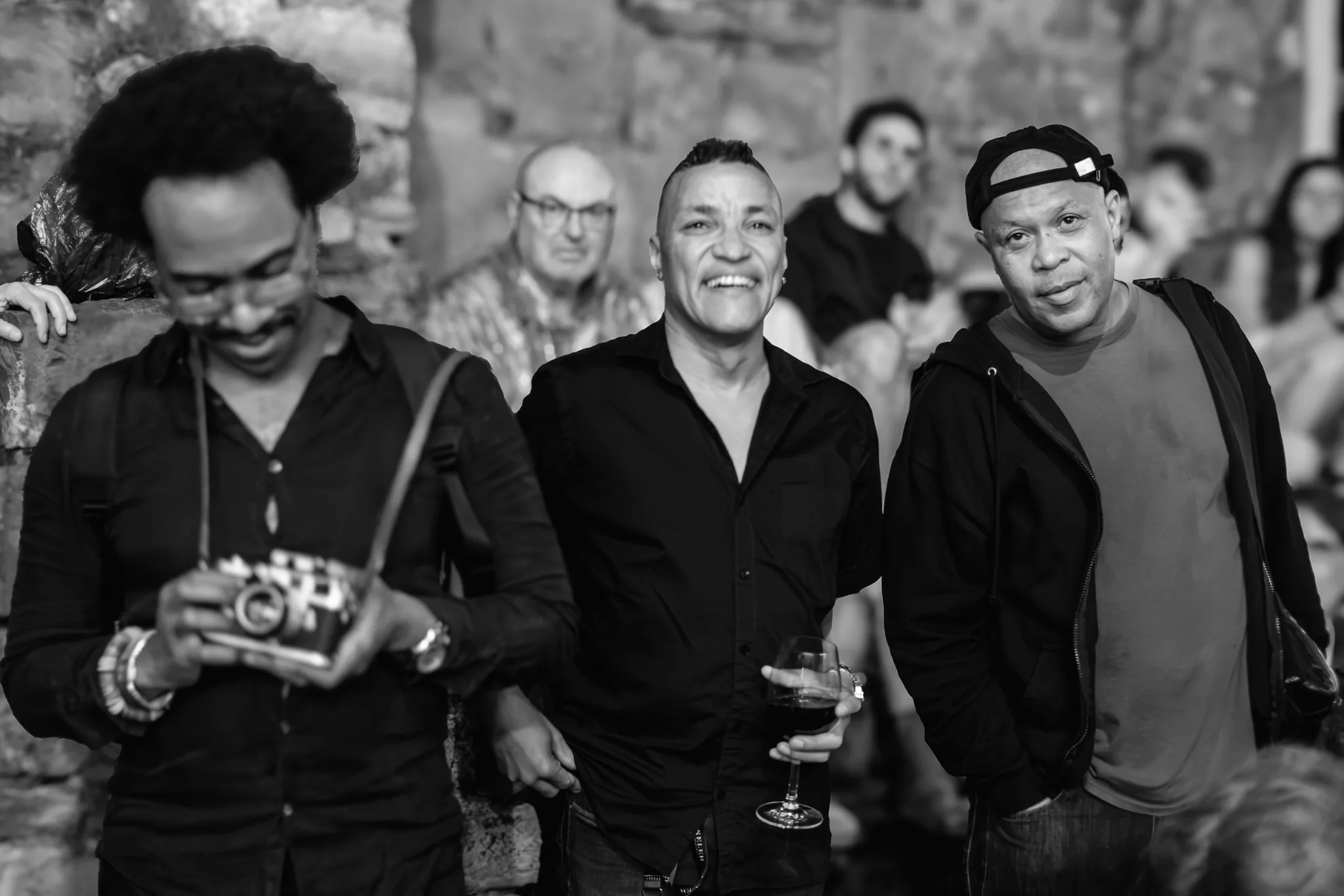 Musicians smiling together, with a camera held by the person at left.