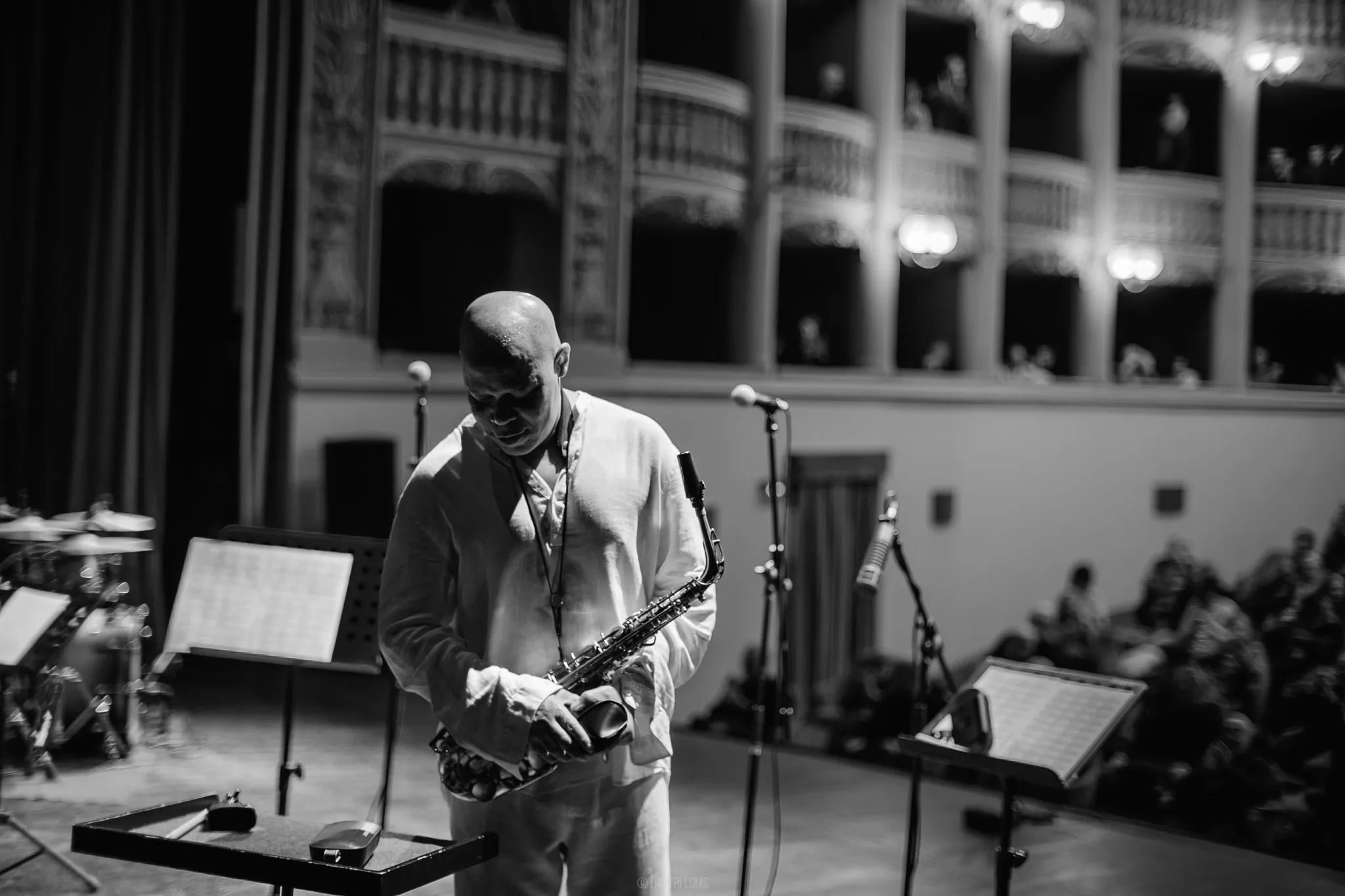 Black-and-white photograph of Steve Coleman holding his alto saxophone in a concert hall.