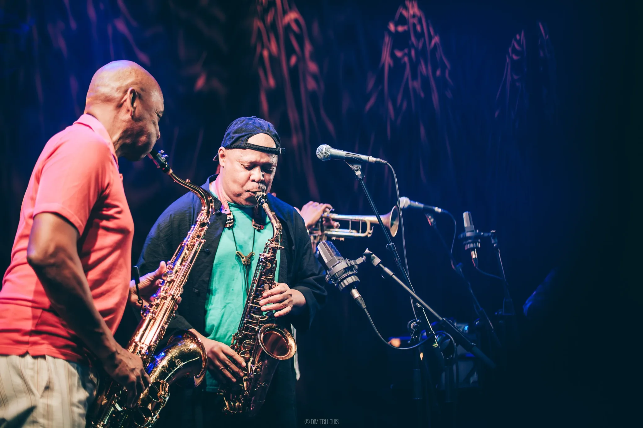 Steve Coleman holding his saxophone and talking with a fellow musician beside a microphone in Ghent.