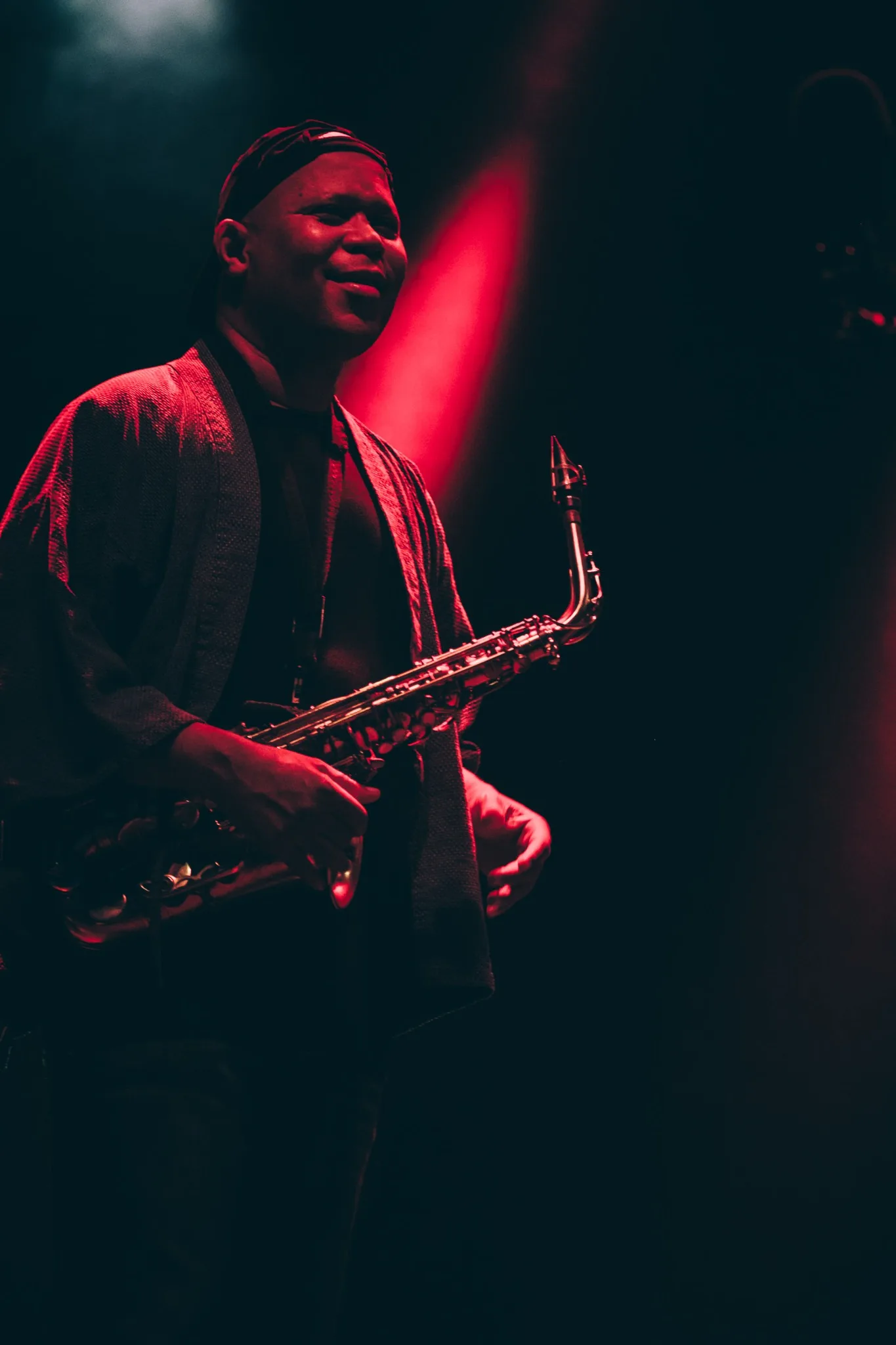 Steve Coleman holding an alto saxophone beneath red and green stage lights.