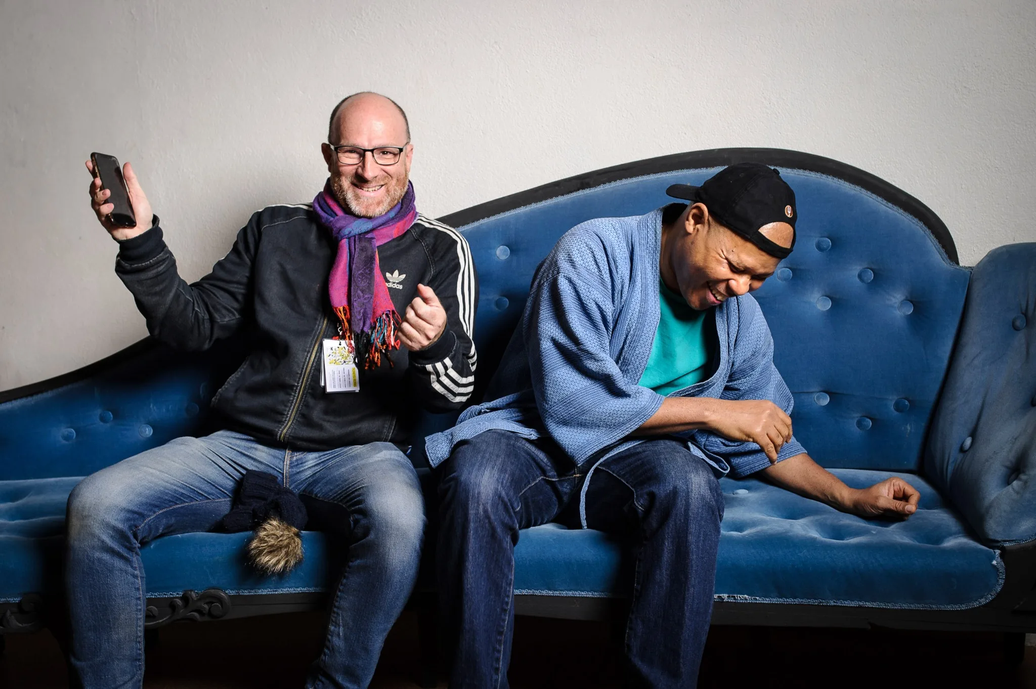 Dimitri Louis and Steve Coleman smiling together on a blue sofa.